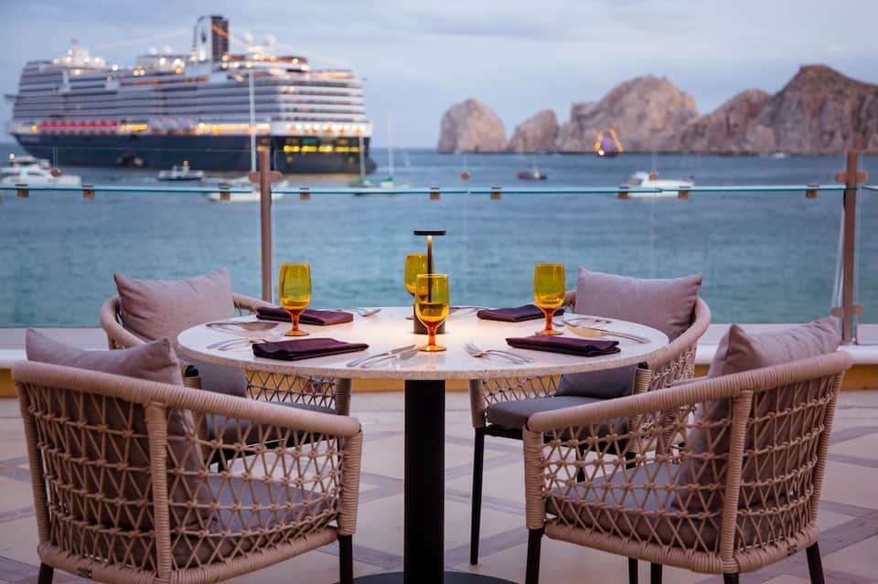Fine dining round table setup on ocean-view terrace with cruise ship and mountains in distance