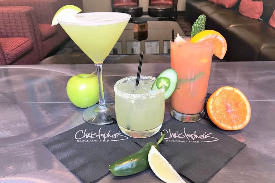 Three colorful cocktails on a bar counter with fresh citrus garnishes at Christopher Restaurant & Bar
