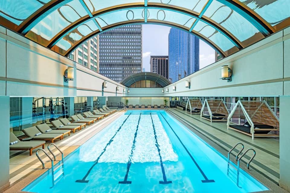 Indoor Olympic-style swimming pool with retractable glass ceiling and urban skyline views