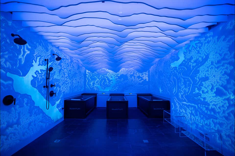 Underwater-themed spa room with blue wave wall murals and black lounge chairs for relaxation
