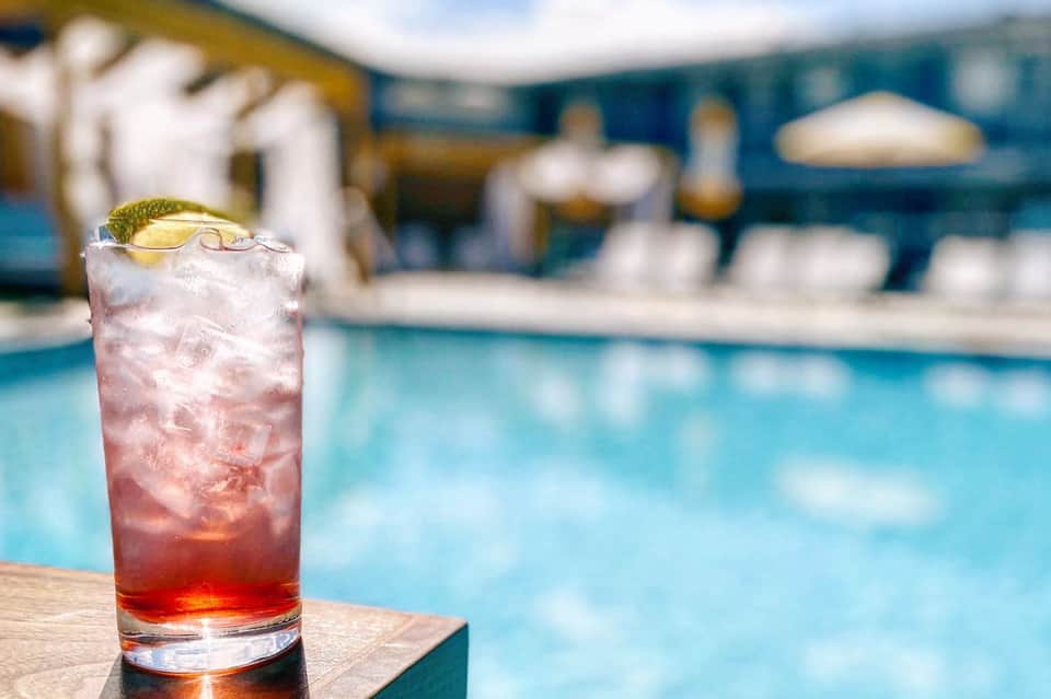 Red cocktail with ice and lime garnish on poolside table with resort in background