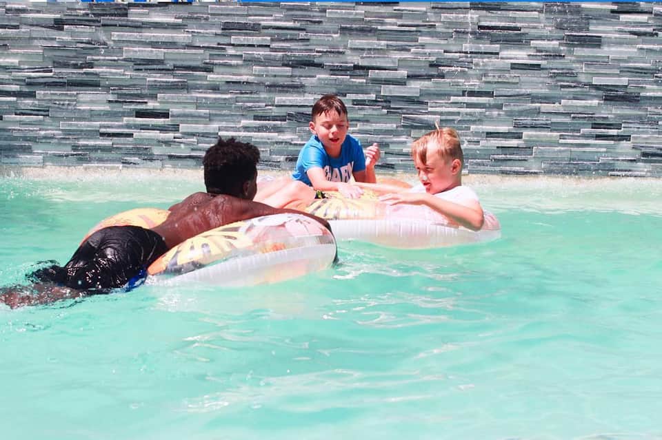 Children and adults floating on inflatable rings in a bright turquoise pool