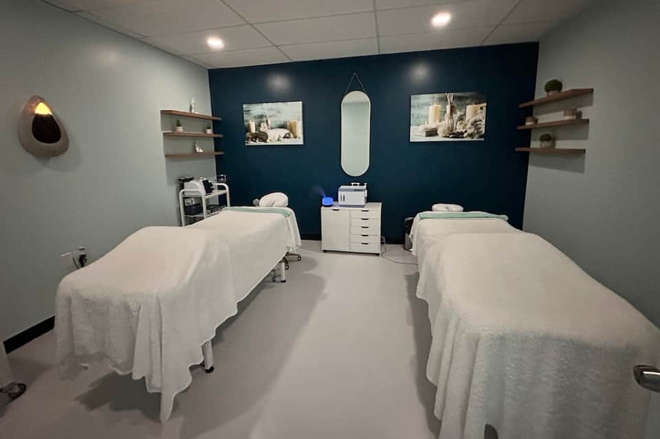 Spa treatment room with two massage tables, dark blue accent wall, and minimalist decor