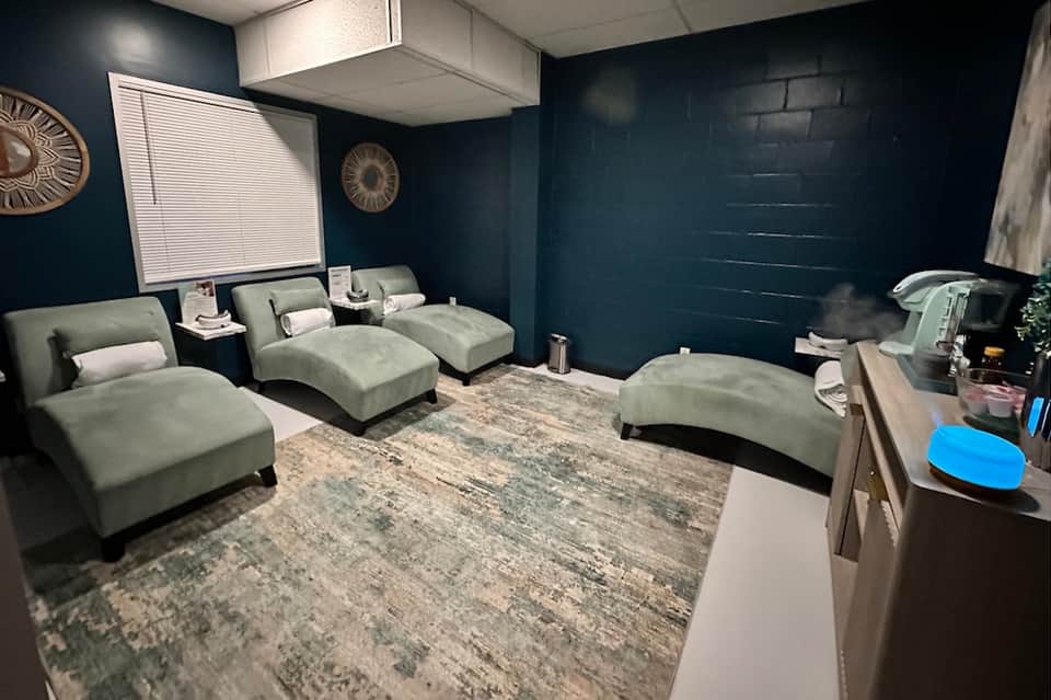 Private spa relaxation room with reclining loungers, dark teal walls, and entertainment screen