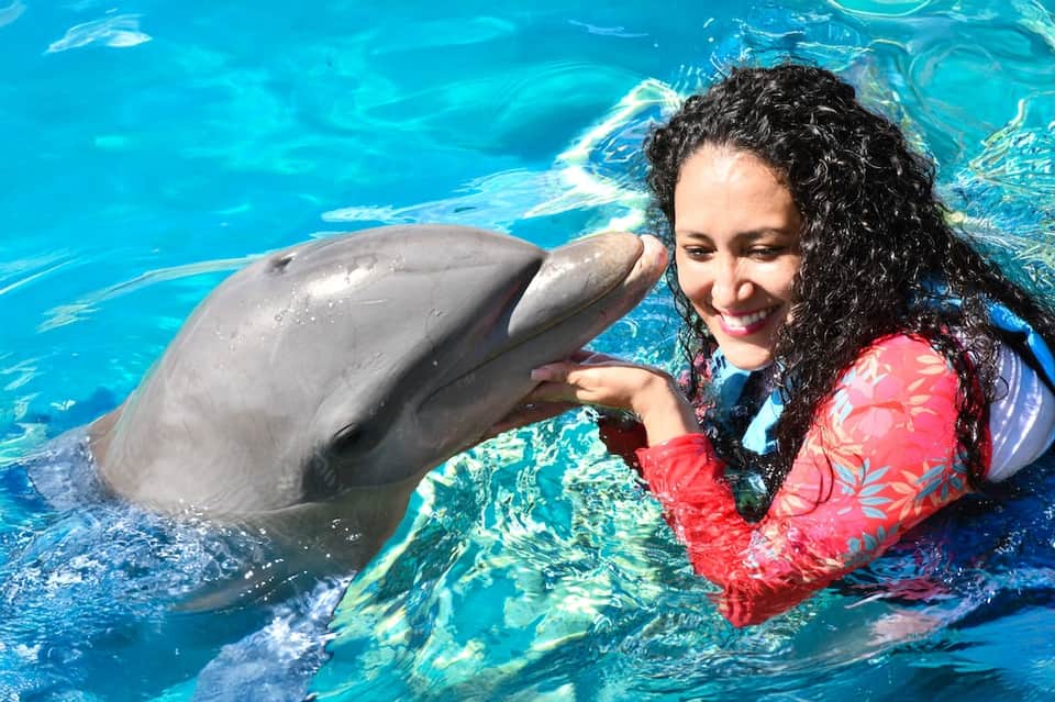 Woman in pink swimsuit playing with a dolphin in bright blue water