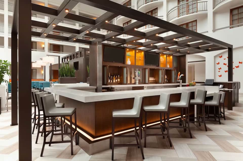 Contemporary hotel bar with brown wood counter, modern seating, and open atrium design