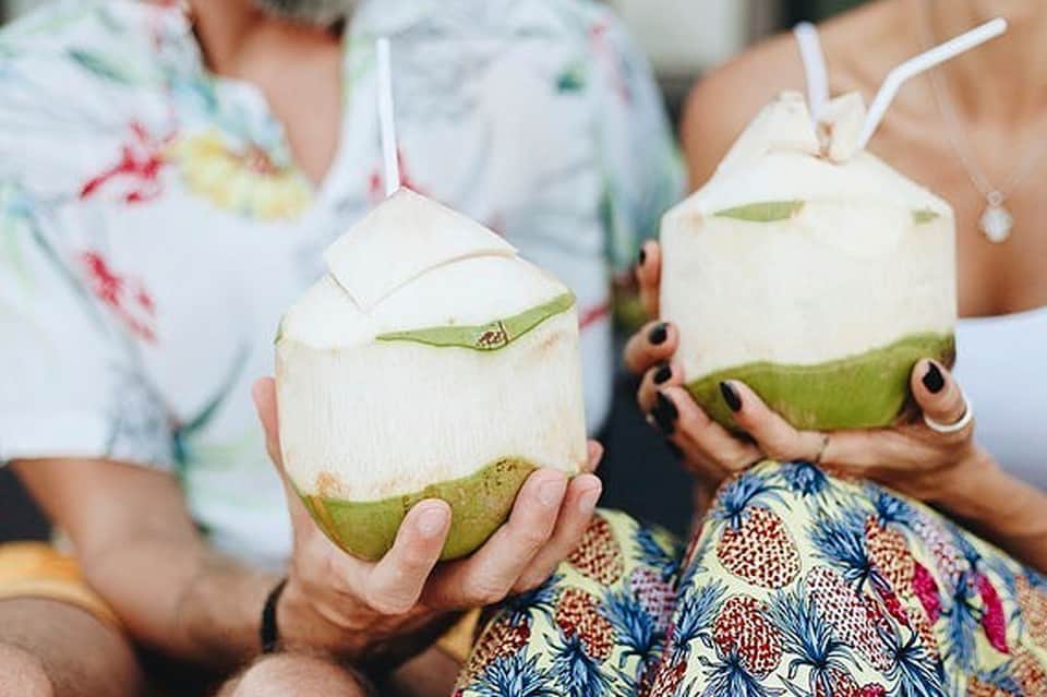 Two people holding fresh young coconuts with straws and green garnish
