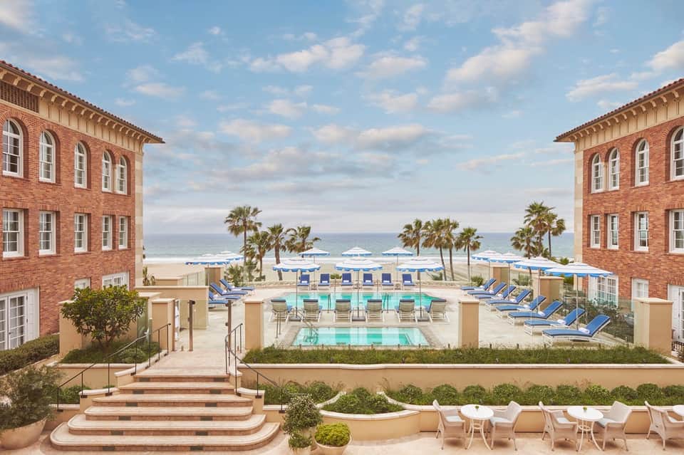 Beachfront resort courtyard with central pool, brick buildings, palm trees, and ocean view