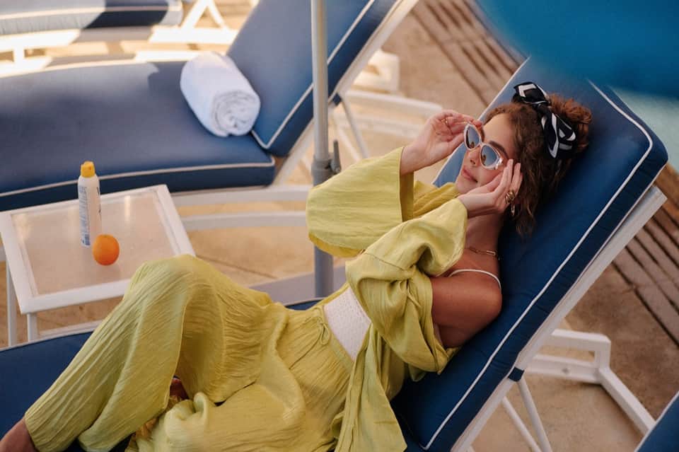 Guest in yellow outfit relaxing on blue lounge chair with sunglasses and fruit drink