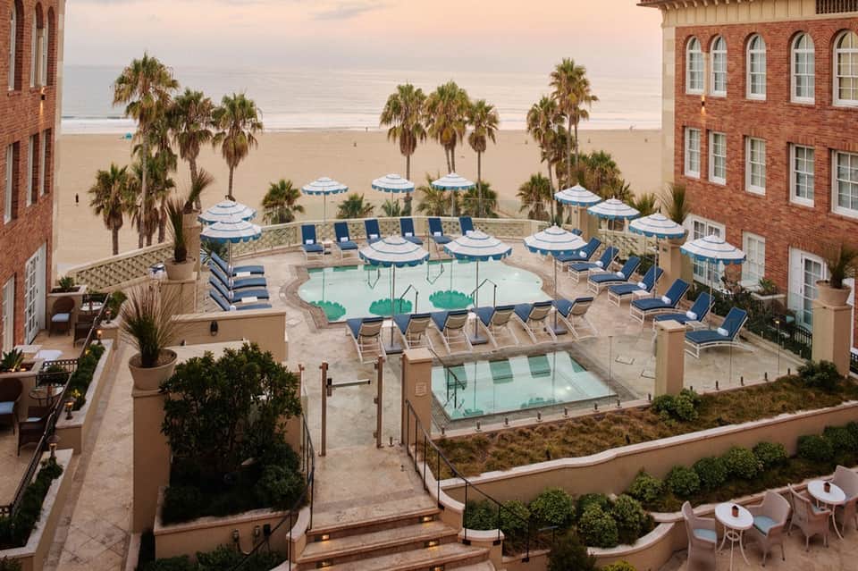 Beachfront resort pool deck with umbrellas, lounge chairs, palm trees, and ocean view