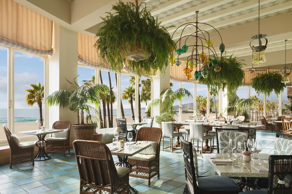 Beachfront dining room with wicker seating, hanging plants, and ocean views