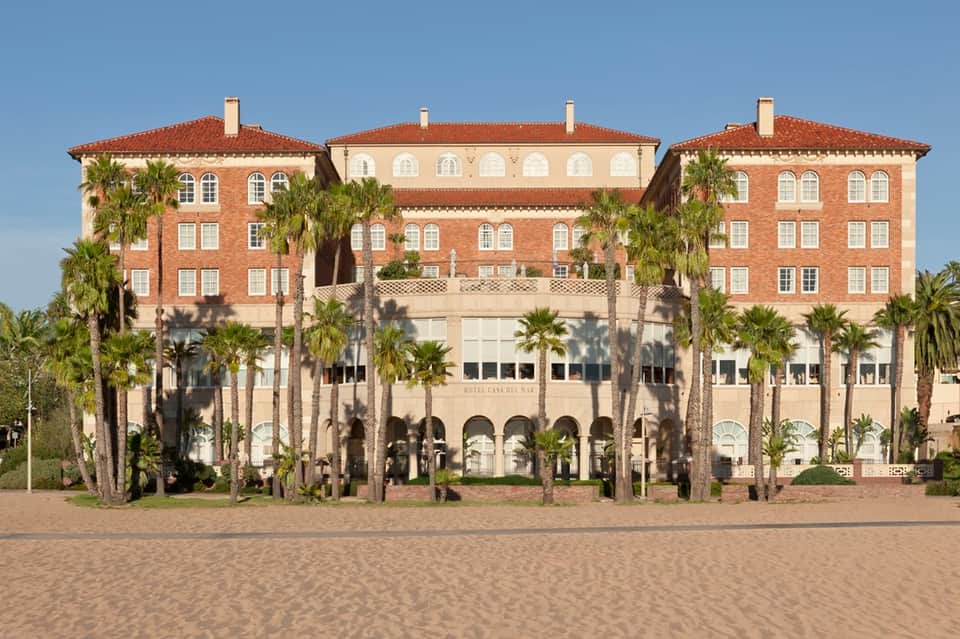 Historic brick and stone hotel building on beach with palm trees and arcades