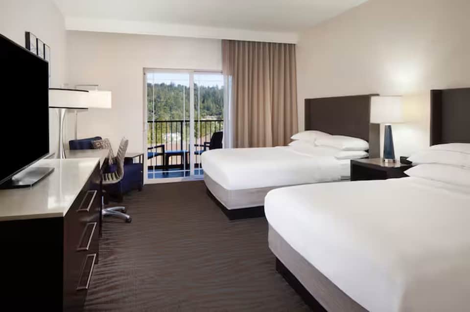 Hotel guest room with two queen beds, desk area, balcony, and forest view with modern furnishings