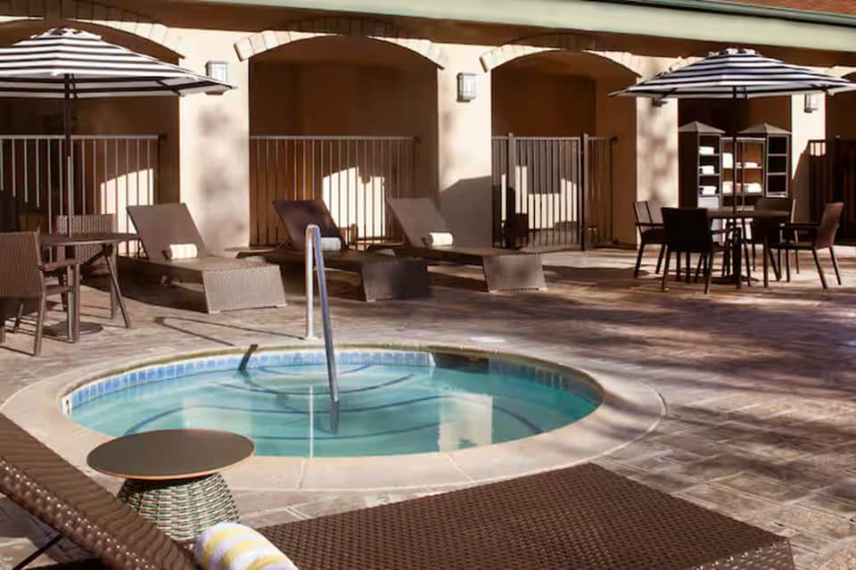 Resort spa courtyard with circular hot tub, arched covered structures, umbrellas, loungers, and architectural columns