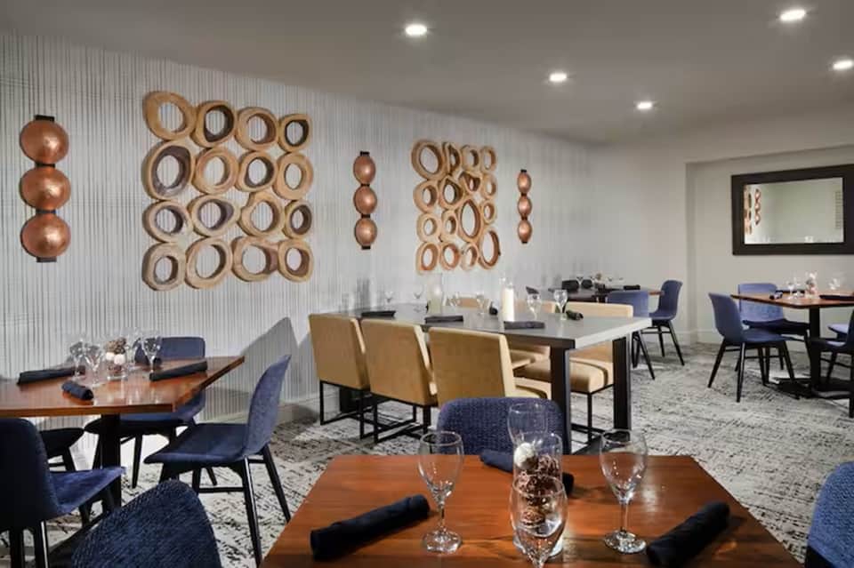 Contemporary dining room with decorative copper wall art, wooden tables, navy chairs, and mirrors