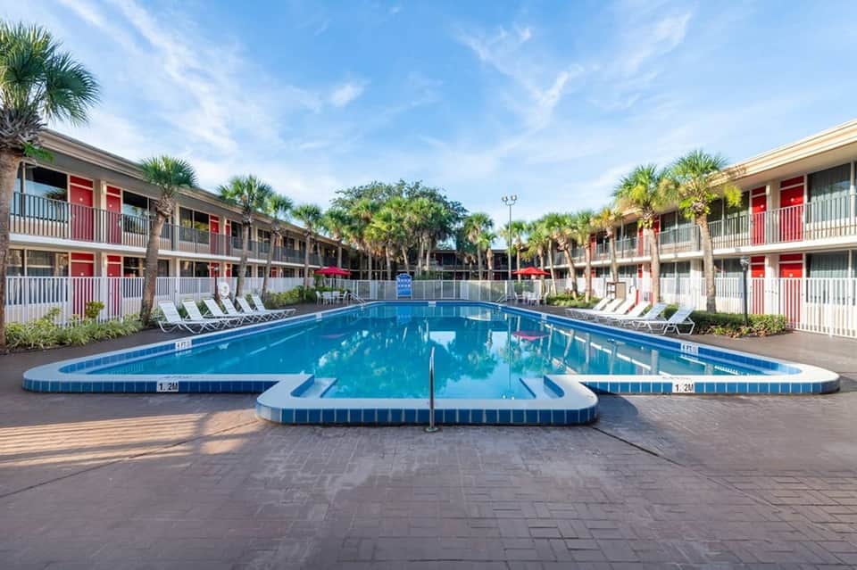 Resort pool with red and white building courtyard, palm trees, and lounge chairs