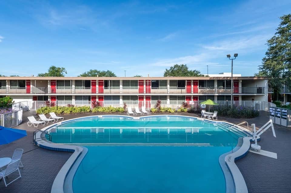 Resort pool area with white lounge chairs and red-door motel-style building backdrop