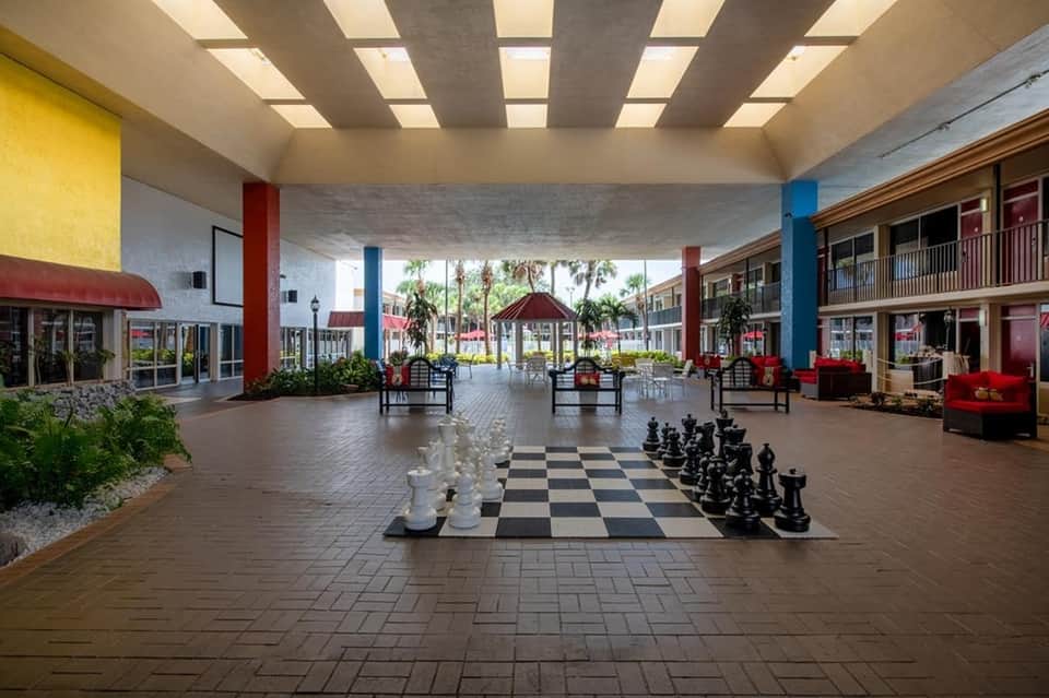 Indoor mall promenade with colorful columns, large chess board, and tropical plants