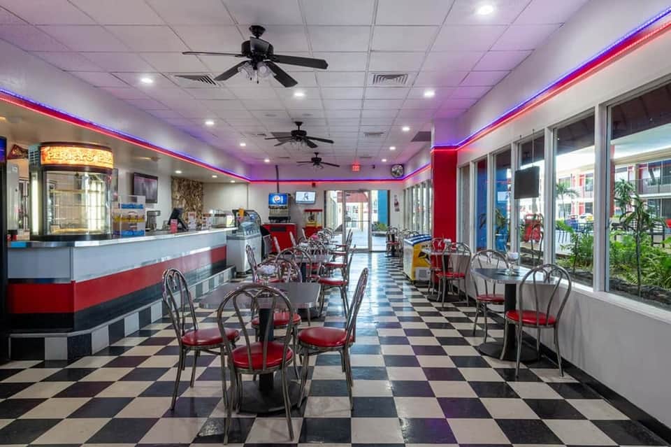 Retro diner interior with red and blue neon ceiling, checkered floor, and classic booth seating