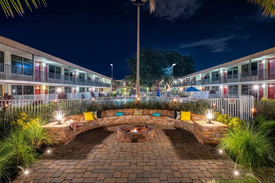 Nighttime resort courtyard with circular stone fire pit, seating, accent lighting, and motel-style building