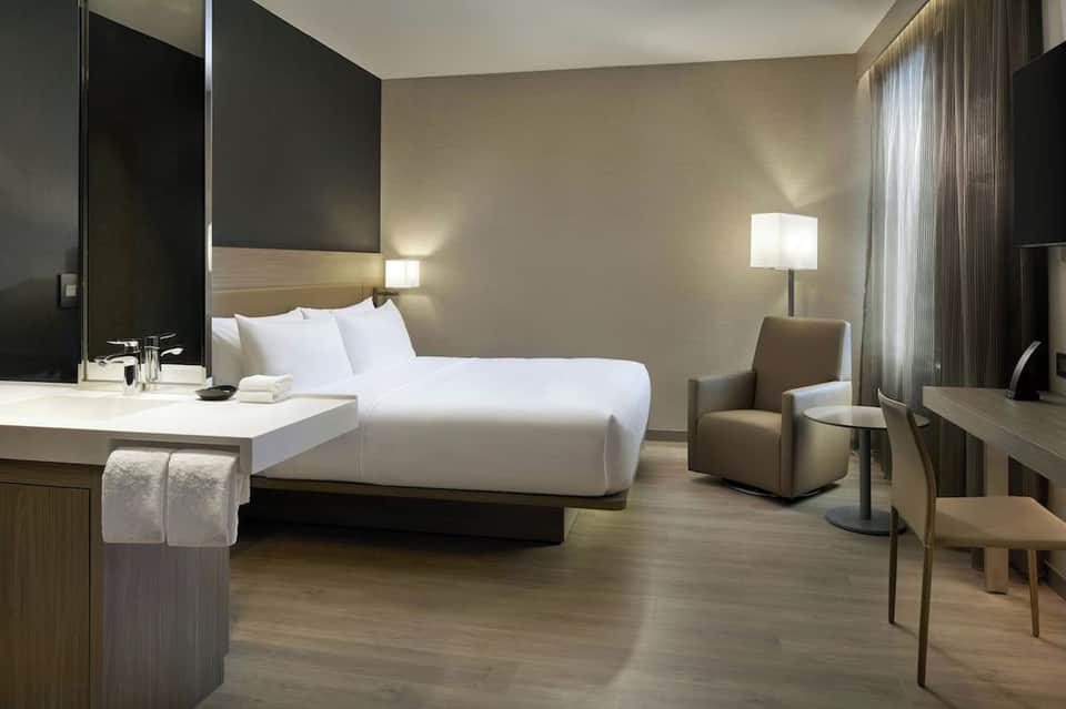 Contemporary hotel room with king bed, white linens, modern desk, and minimalist neutral decor