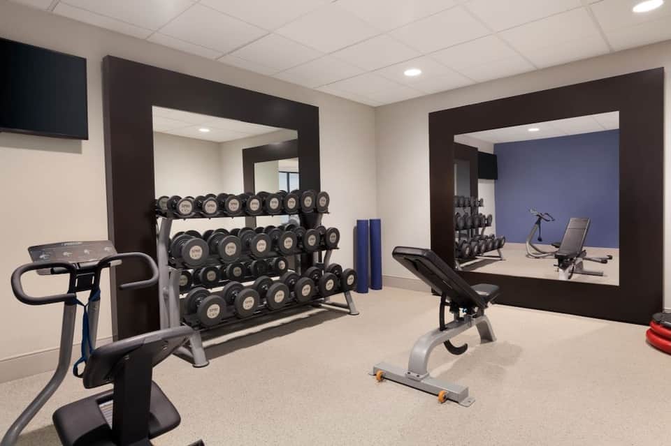Well-equipped fitness center with dumbbell racks, exercise bike, and mirror wall