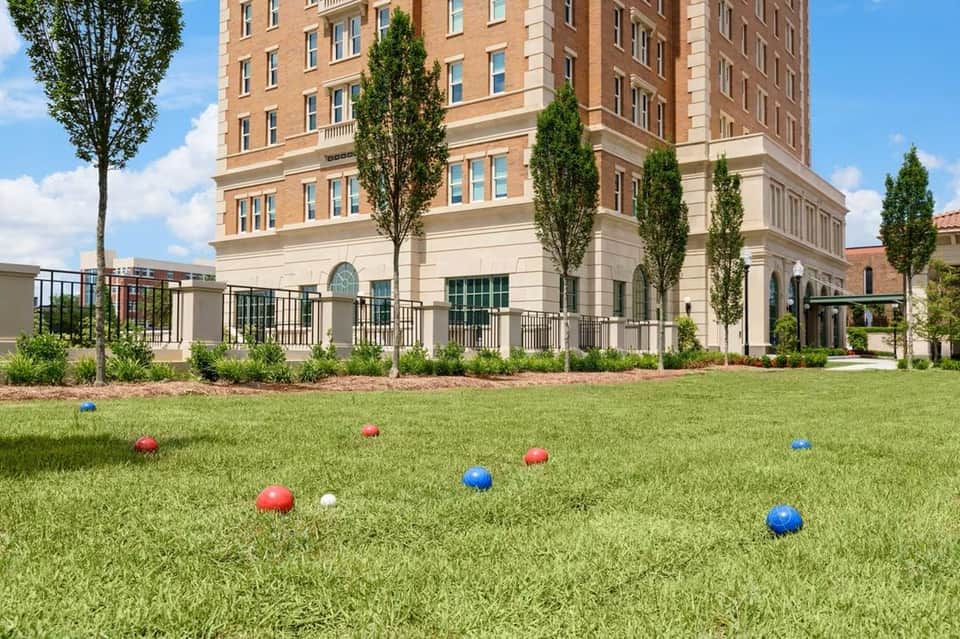 Brick hotel exterior with manicured lawn, black railing and colorful bocce balls scattered