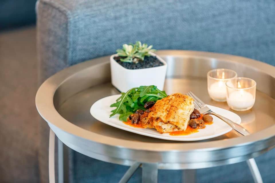 Fine dining plate with herb-crusted protein, fresh arugula, and sauce on round metal table with candles and succulent