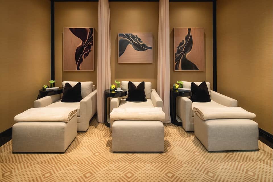 Spa relaxation room with three cream chaise lounges, gold walls, and framed abstract artwork