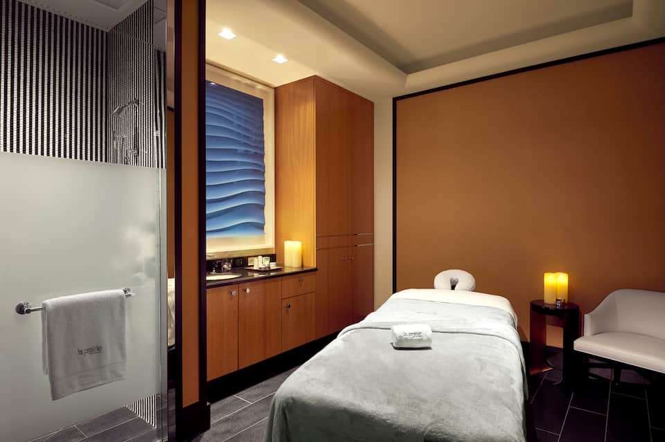Spa treatment room with massage bed, wooden cabinetry, and warm ambient lighting