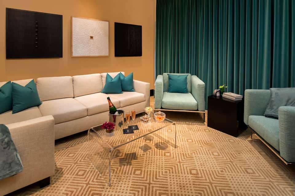 Modern hotel suite with cream sectional sofa, teal accents, and orange accent wall
