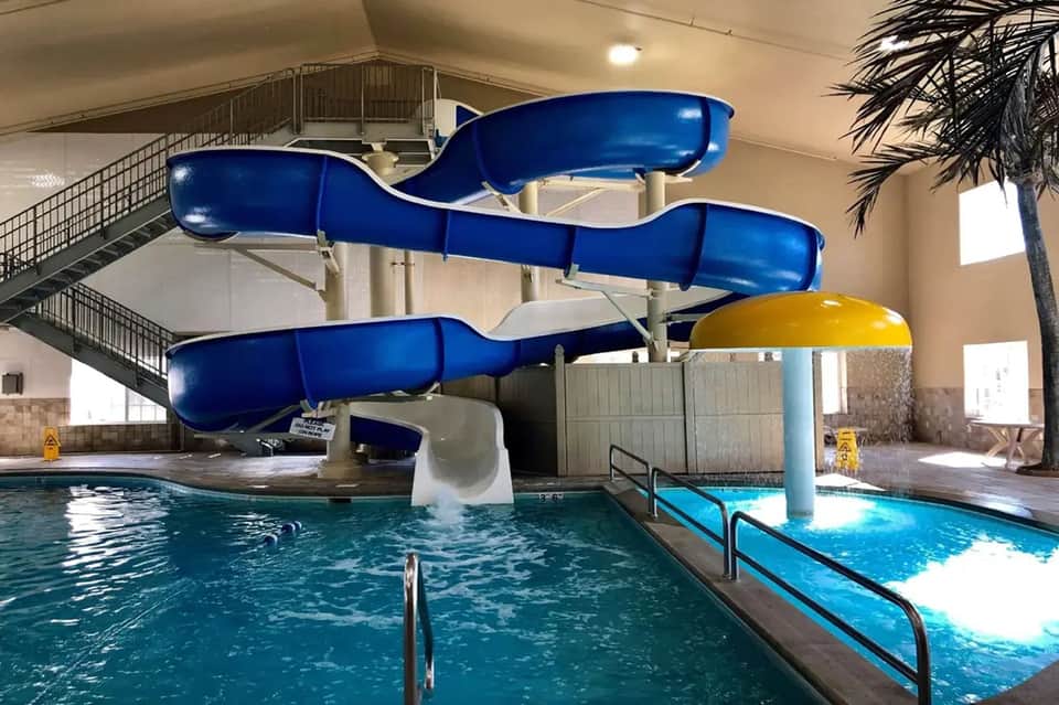 Indoor water park with blue twisting slides, pool, and palm trees in bright atrium space