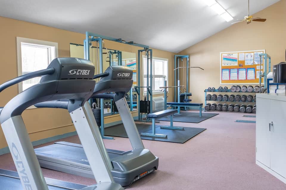 Modern fitness center with treadmills, weight equipment, dumbbells, and mirrors in bright, well-lit facility.