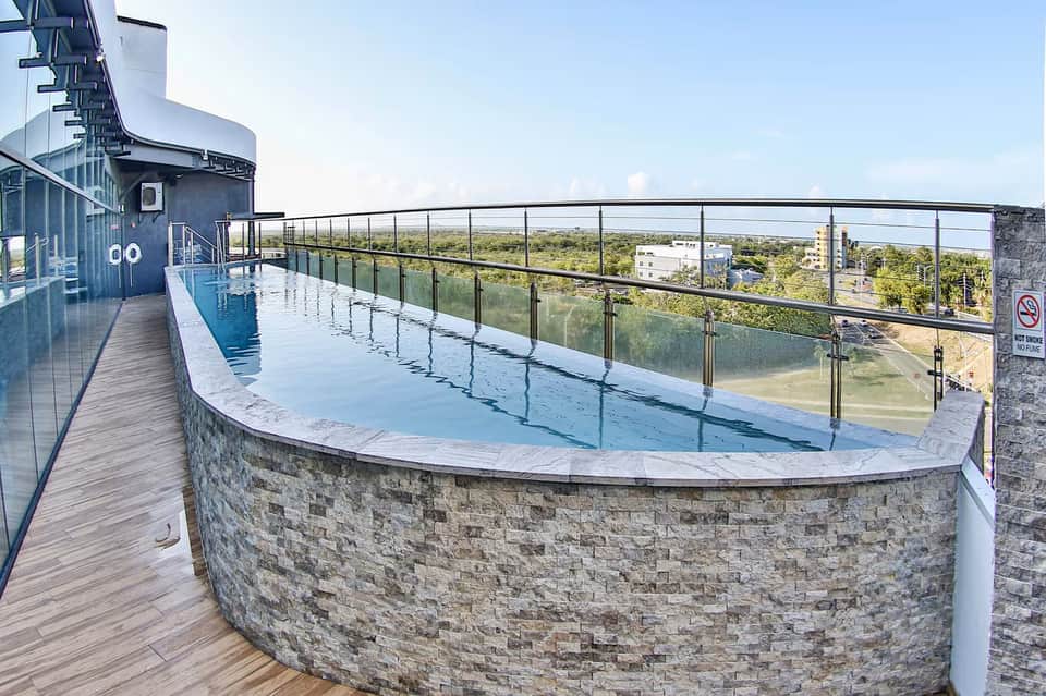 Rooftop curved pool with glass railing, wooden deck, landscape views, and modern architecture