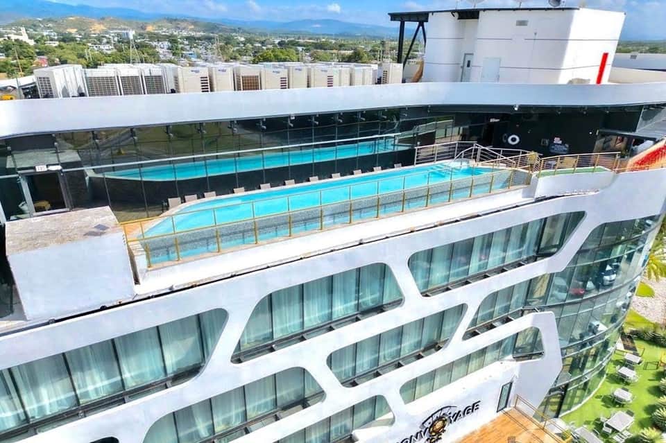 Modern high-rise hotel with rooftop turquoise pool, glass balconies, mountain views, and contemporary architecture