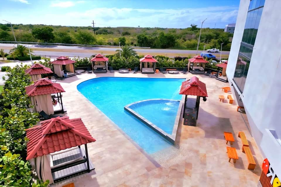 Resort pool with red cabana umbrellas, turquoise water, spa gazebos, and scenic waterfront views