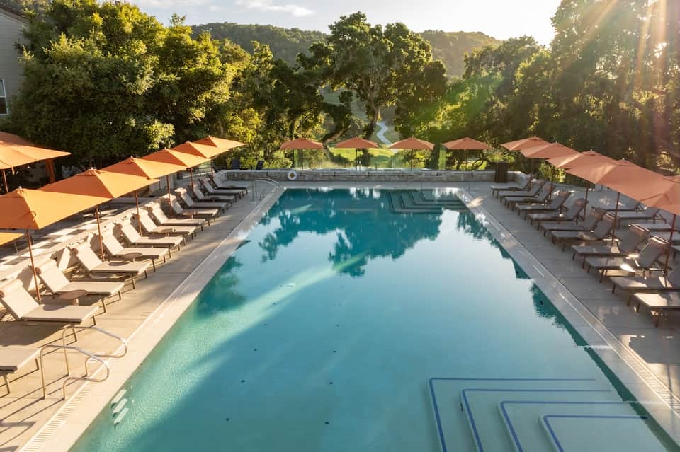 Resort lap pool with colorful umbrellas lining both sides, lounge chairs, and wooded hillside view
