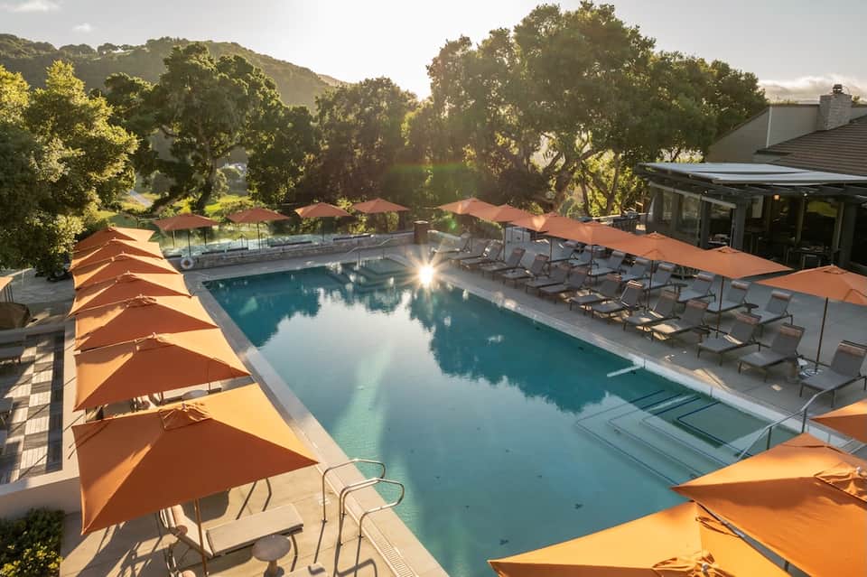 Resort pool with orange umbrellas, lounge chairs, and surrounding oak trees at golden hour
