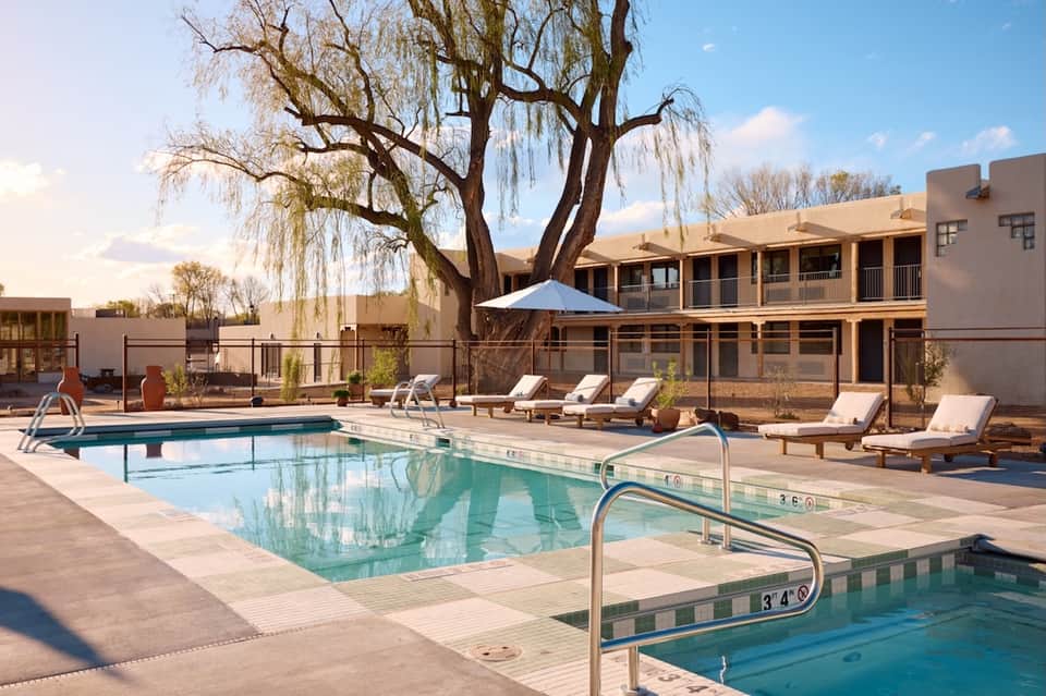 Resort pool courtyard with lounge chairs, weeping willow tree, southwestern-style buildings, and spa facility