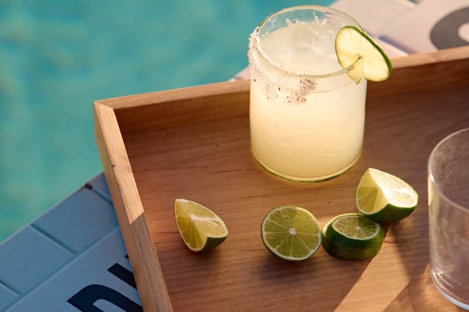 Margarita cocktail with lime garnish on wooden tray by turquoise pool