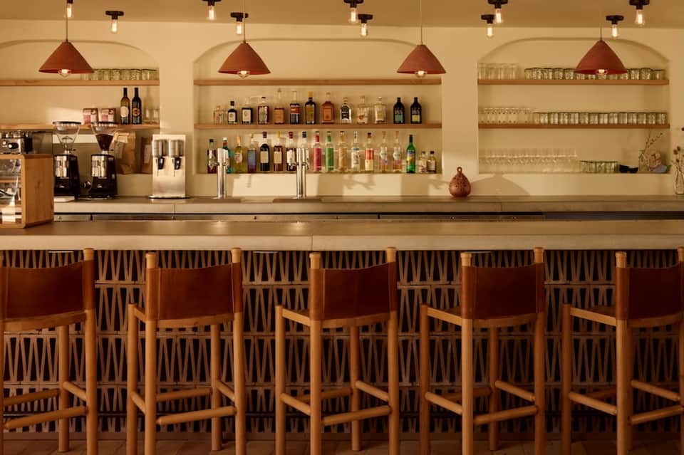 Upscale bar with wooden chairs, copper pendant lights, and shelves stocked with spirits and glassware