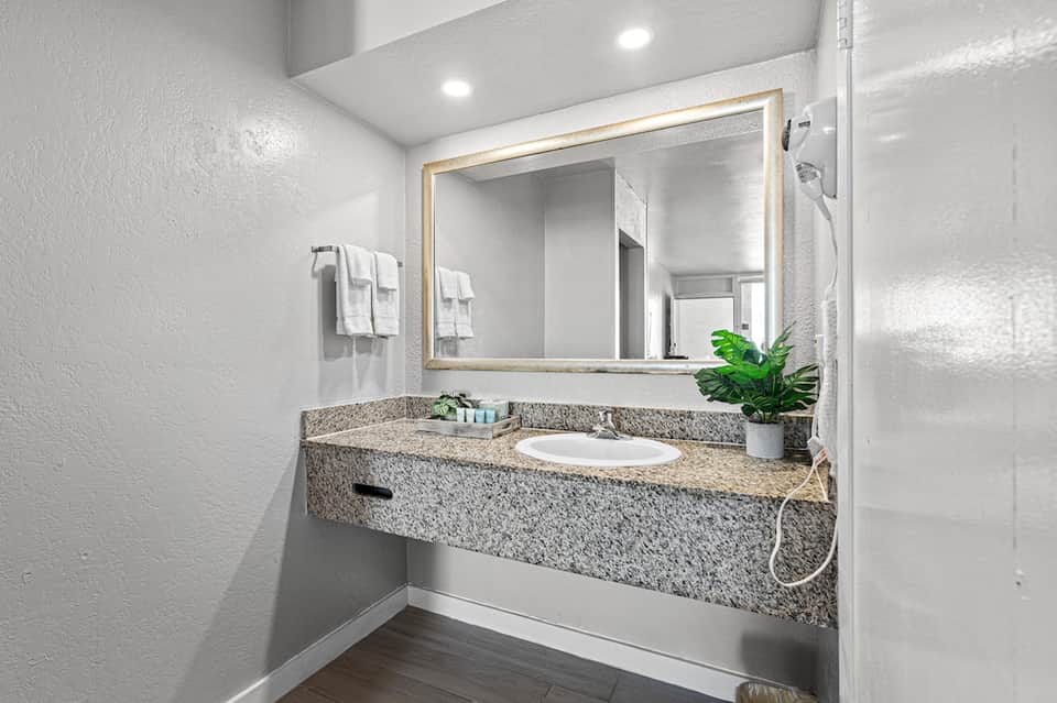 Clean bathroom vanity with granite countertop, illuminated mirror, and white towels