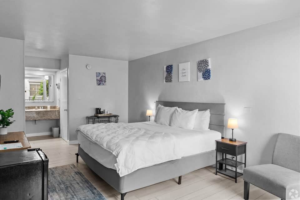 Modern hotel bedroom with gray upholstered bed, white linens, and ensuite bathroom
