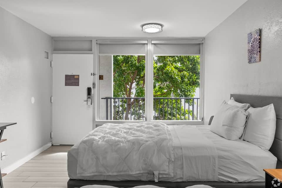Bright hotel bedroom with modern furnishings and sliding glass door overlooking trees and balcony