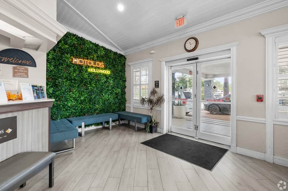Hotel lobby entrance with green living wall, neon signage, blue seating, and reception desk