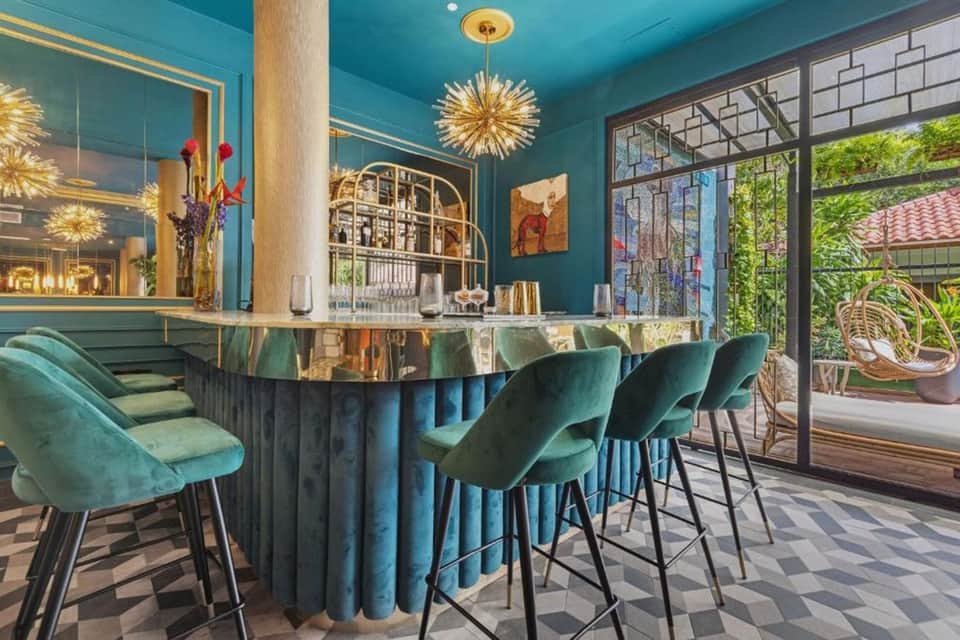 Upscale teal lounge bar with gold fixtures, velvet chairs, and tropical garden views