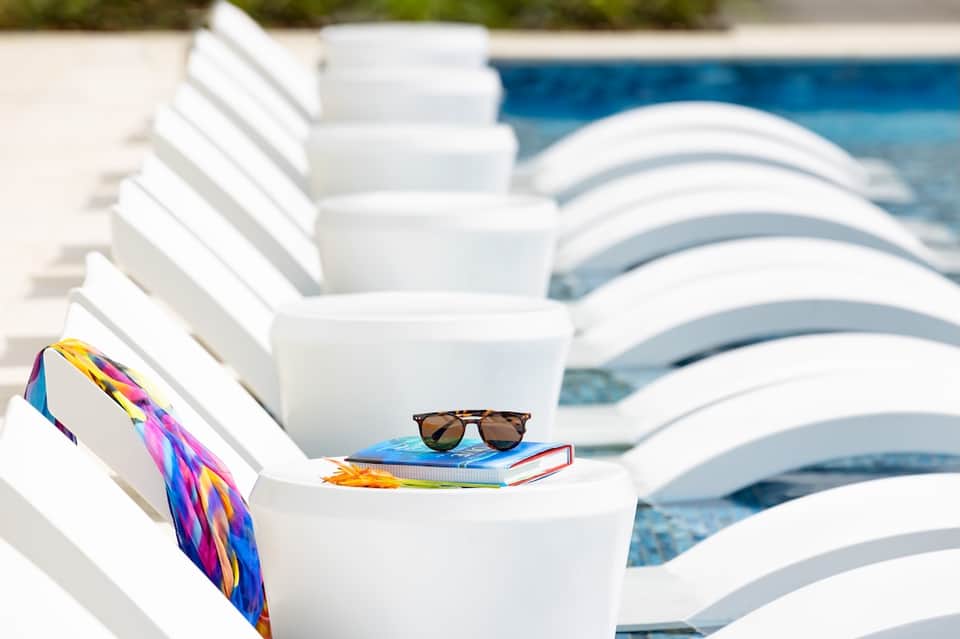 White poolside loungers with colorful scarf and sunglasses beside turquoise swimming pool