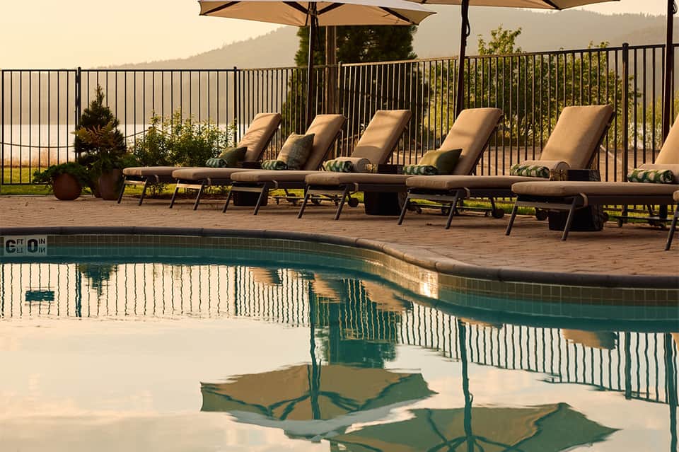 Mountain resort pool with lounge chairs, umbrellas, scenic valley views, and railing