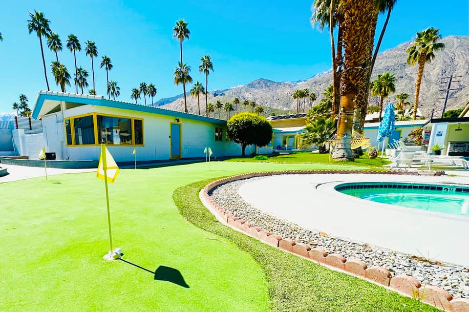 Retro-style poolside building with bright colors, manicured lawn, and palm tree landscape