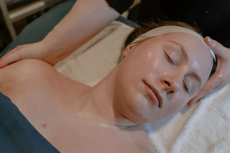 Spa therapist performing facial treatment on client lying down with white headband